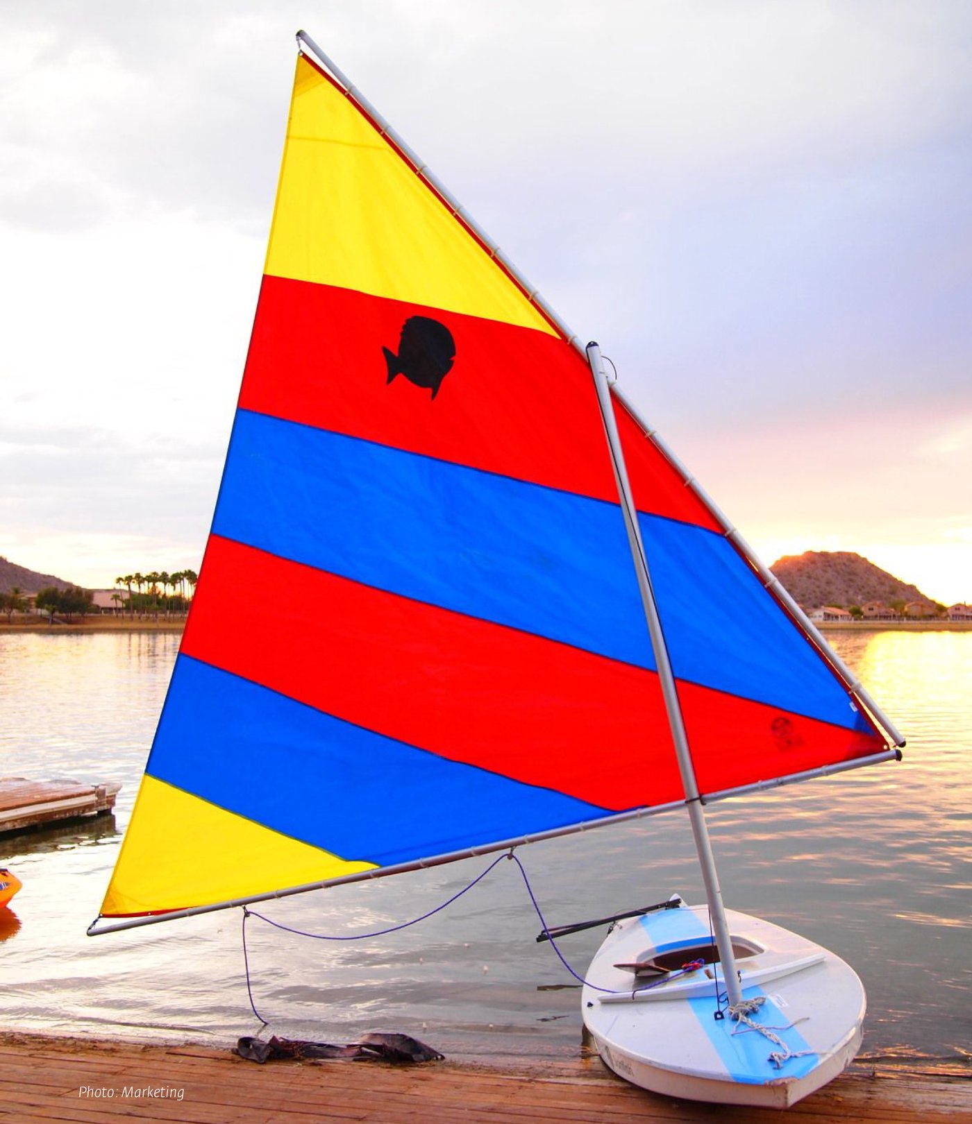 Sunfish sailboat with the original logo: a plain black fish silhouette printed on a red, yellow and blue striped sail